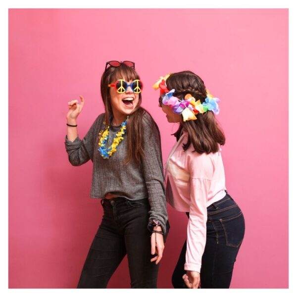 Two girls pose with props in front of a pink backdrop